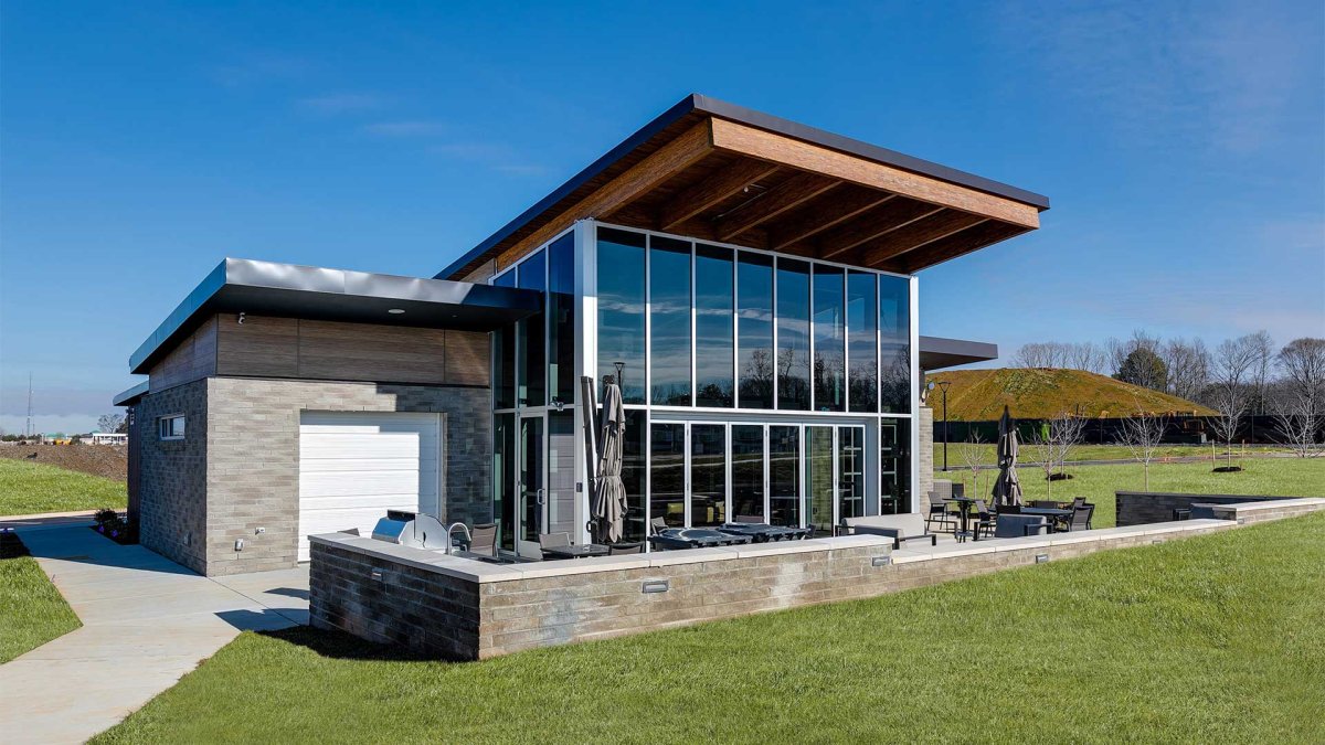 Exterior of the modern Connexion Clubhouse at Wescott by HHHunt Homes, showcasing floor-to-ceiling glass windows, outdoor seating area, and sleek architectural design surrounded by green landscaping.