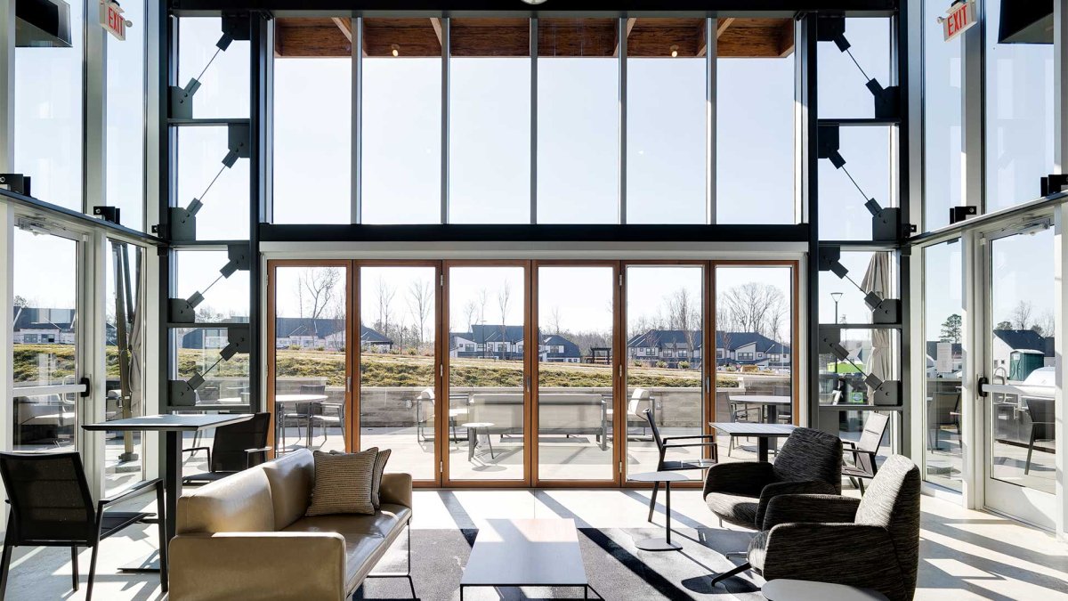 Interior view of the Wescott Connexion Clubhouse lounge by HHHunt Homes, featuring floor-to-ceiling windows, modern seating, and a seamless transition to the outdoor patio with views of the community.