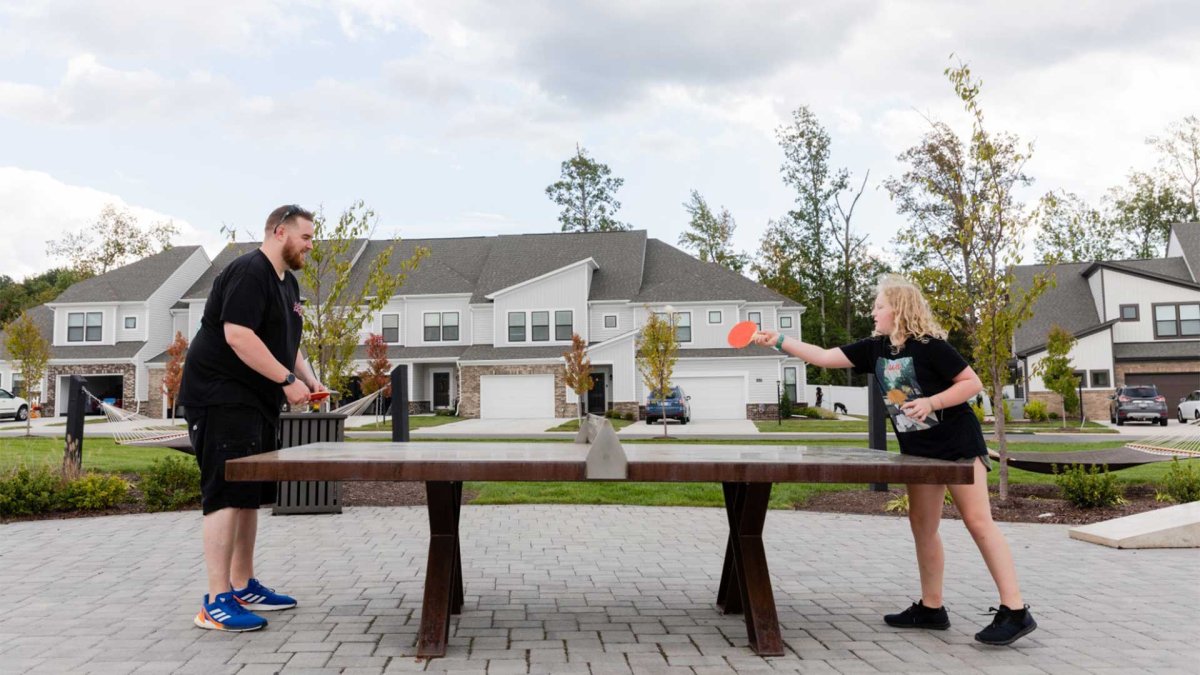 Residents enjoying a game of ping pong outdoors at Wescott by HHHunt, with townhomes and landscaping in the background on a paved community patio.