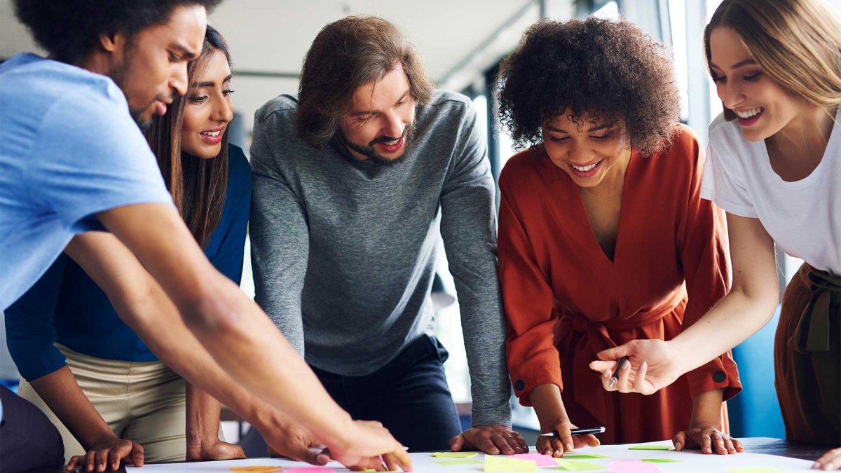 Group of professionals collaborating around a table with sticky notes in a modern office setting, engaged in a team brainstorming session.