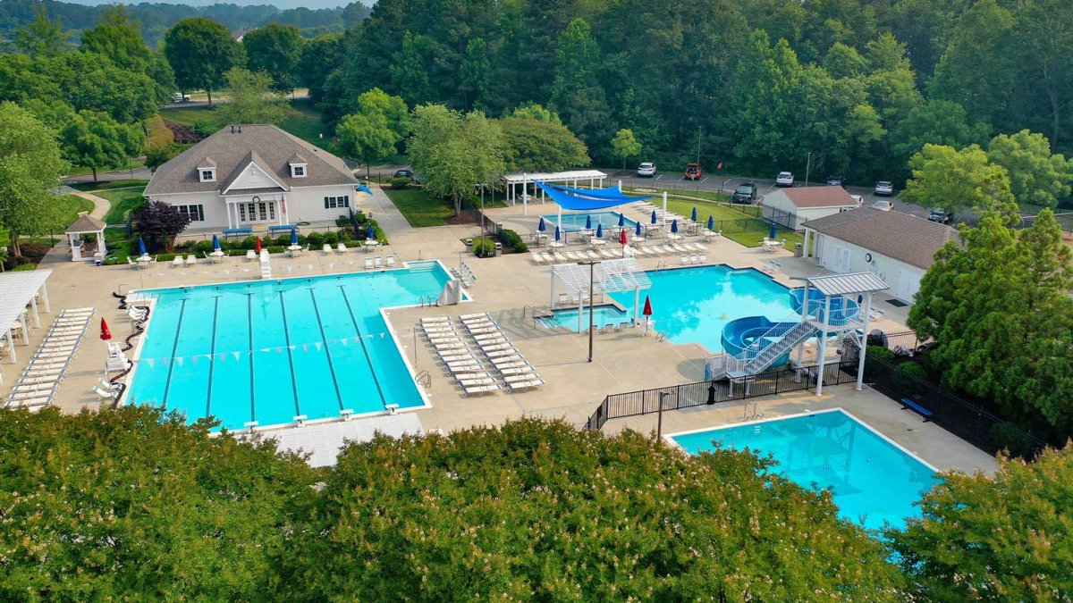 Aerial view of the pool complex at The Pointe at Twin Hickory by HHHunt Homes, featuring lap lanes, leisure pools, water slide, and clubhouse surrounded by mature trees