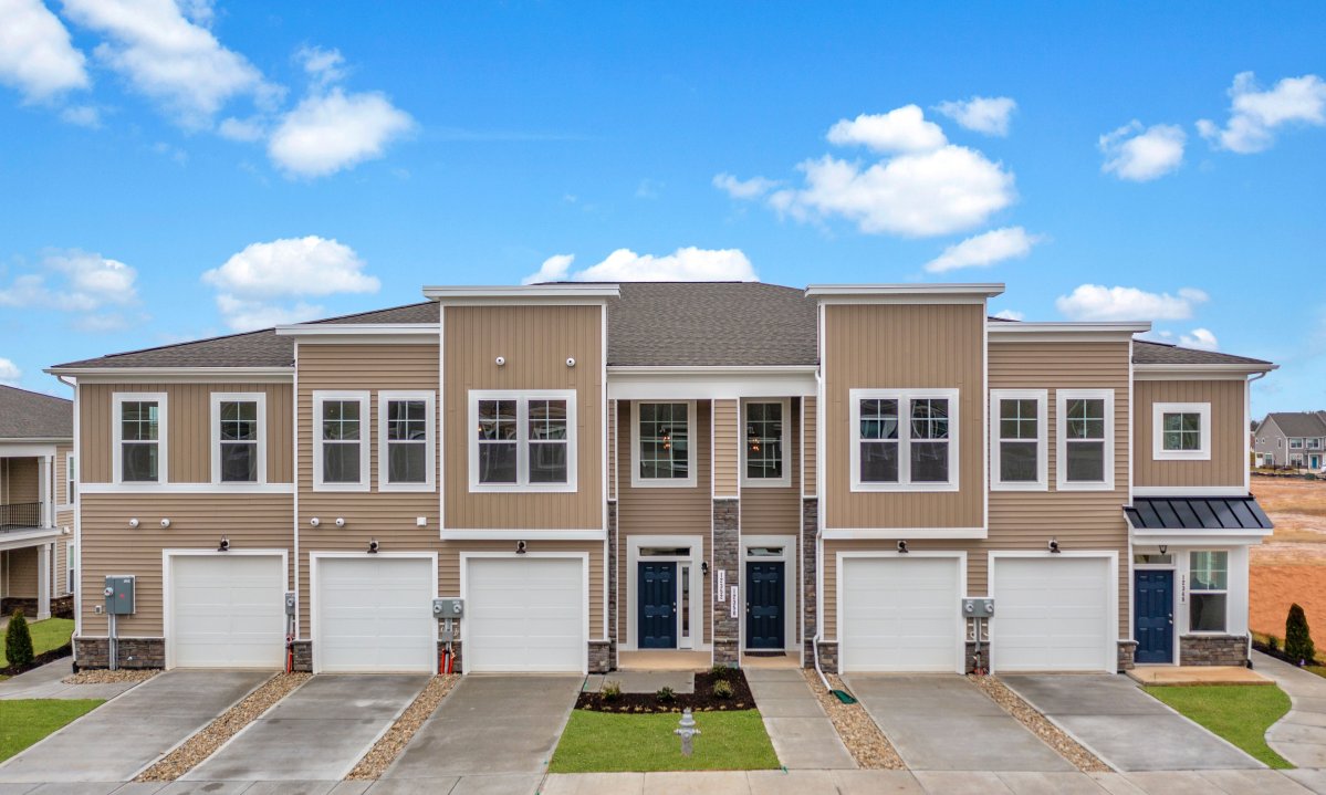 Wescott Condos streetscape by HHHunt Homes, showcasing modern multi-level townhome-style condominiums with attached garages and tan siding.