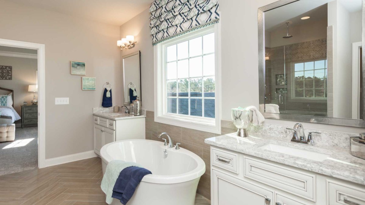 Ensuite bathroom in the Crawford floor plan by HHHunt Homes at The Summit At Morgan Ridge, featuring a freestanding soaking tub, dual vanities with marble-style countertops, herringbone tile flooring, a large framed mirror, and a glass-enclosed walk-in sh