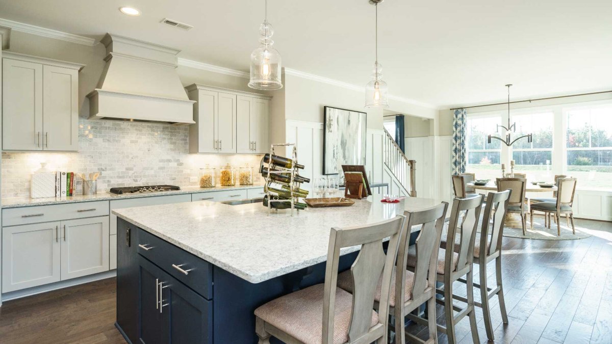 Kitchen and dining room in an HHHunt Home at The Summit At Morgan Ridge, featuring a large island with seating, navy lower cabinets, quartz countertops, stainless steel appliances, pendant lighting, and a bright dining area with large windows and modern c