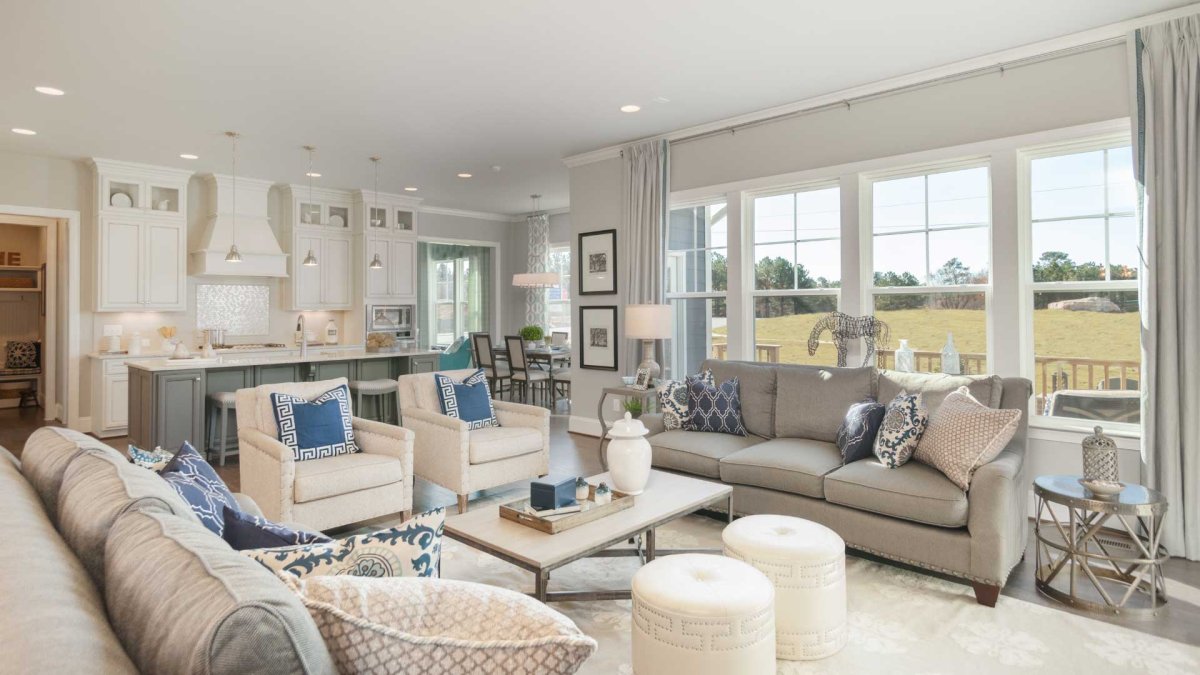Living room and kitchen in an HHHunt Home at The Summit At Morgan Ridge featuring an open-concept layout with large windows, neutral-toned furniture with blue accents, a spacious kitchen island with pendant lighting and bar seating, white cabinetry, and a