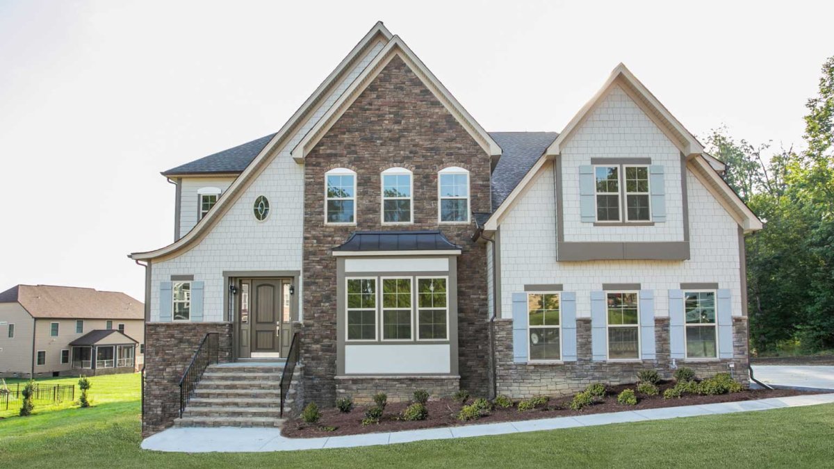 Exterior of the Buckingham floor plan, European A elevation, by HHHunt Homes at The Summit At Morgan Ridge, featuring stone and shake siding, light blue shutters, arched windows, a steep gable roofline, and an elevated front entry with a front door framed