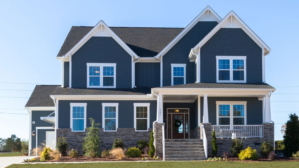 Exterior of the Latham floor plan, Heritage slideload garage elevation, by HHHunt Homes at The Summit At Morgan Ridge, featuring dark blue shake and lap siding, stone water table, white trim, a covered front porch with tapered columns on stone piers, and 