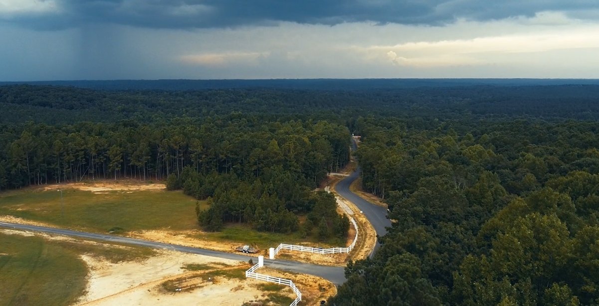 Overhead drone photo of a grass field and a road going through dense woods at Magnolia Acres