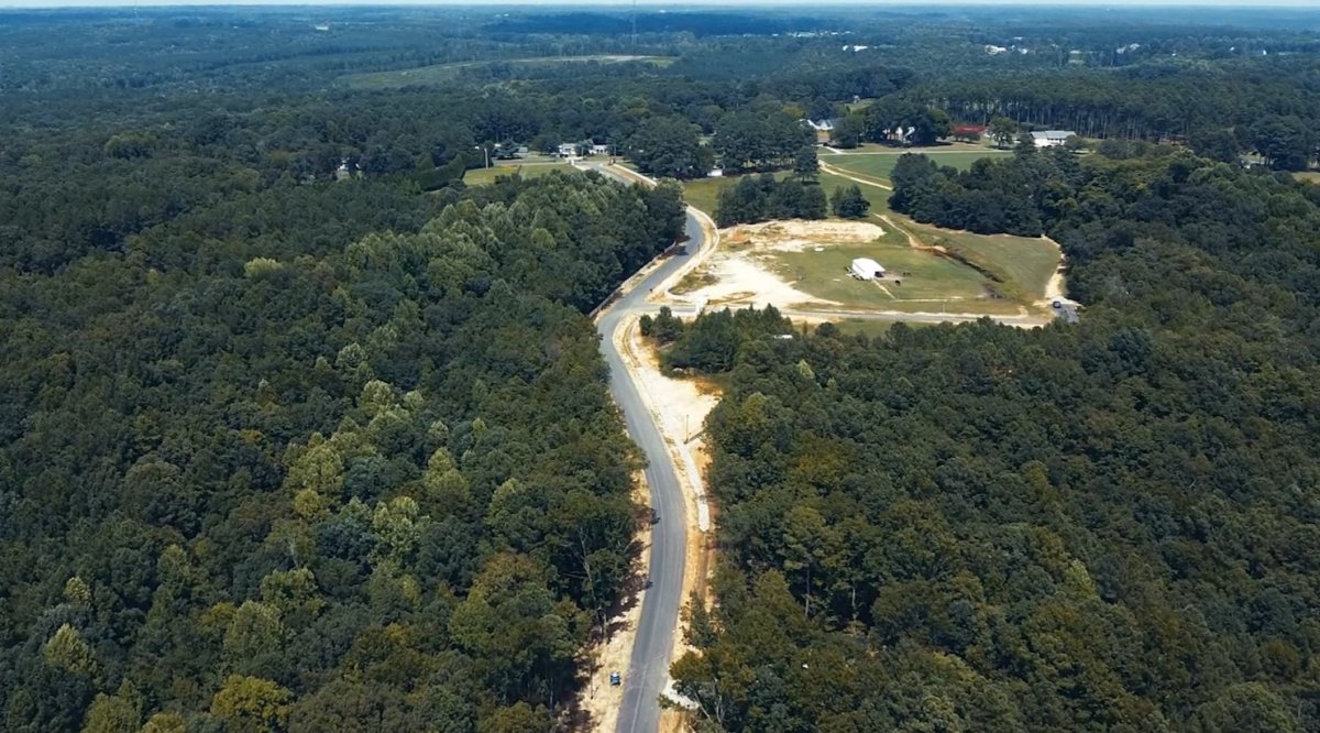 Overhead drone photo of a new road going through dense dark green woods. The beginning of the construction of Magnolia Acres.
