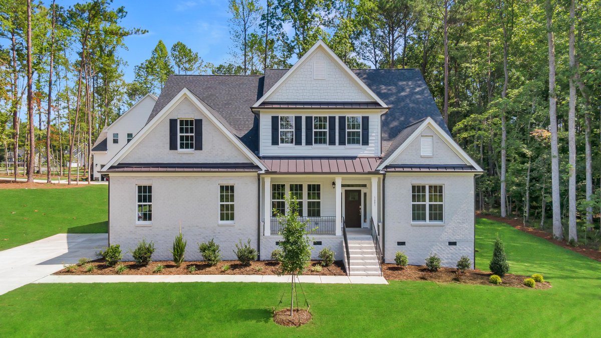 Exterior of the Crawford floor plan, Heritage A elevation, by HHHunt Homes at The Summit At Morgan Ridge, featuring beige brick and shake siding, black shutters, covered front porch with columns, and a landscaped front yard with young trees and shrubs.