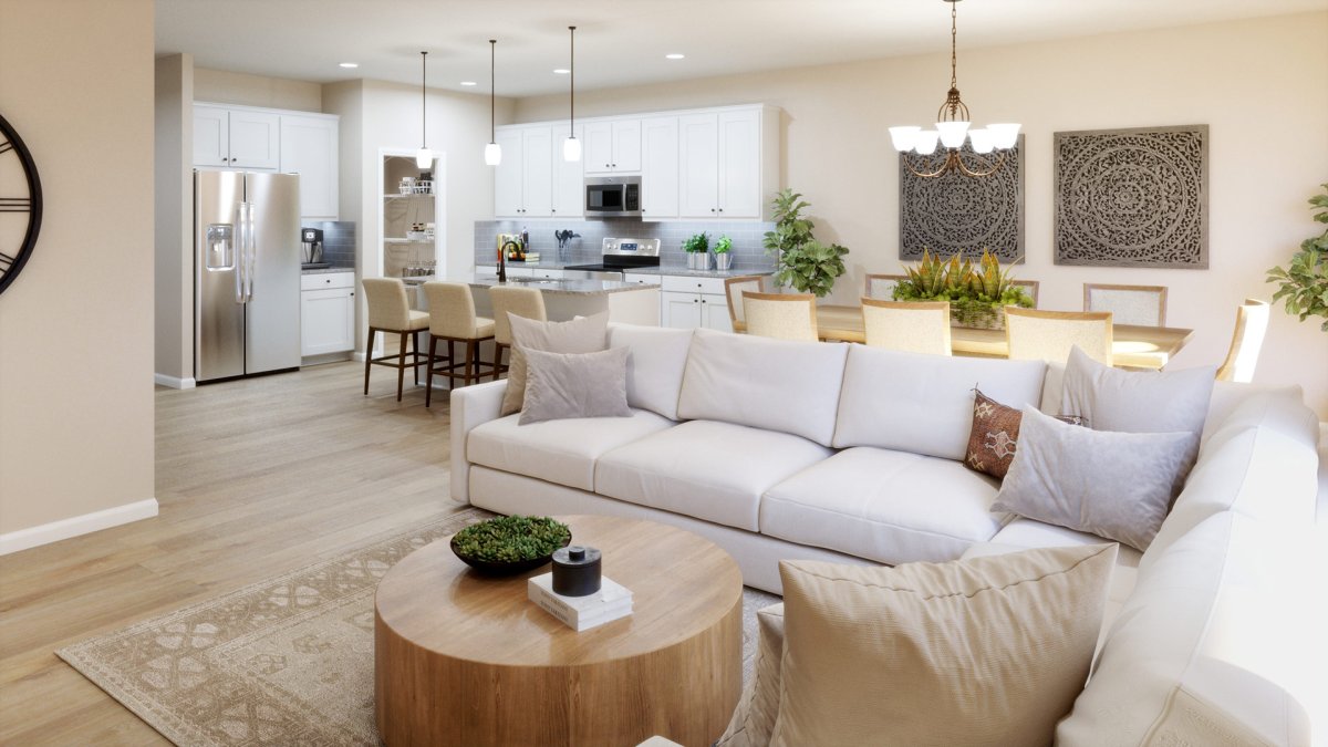 Family room in the Maxwell floor plan by HHHunt Homes at Qualla Trace, featuring an open-concept layout with a large sectional sofa, wood coffee table, adjacent dining area with chandelier, and a white kitchen with pendant lighting, island seating, and st