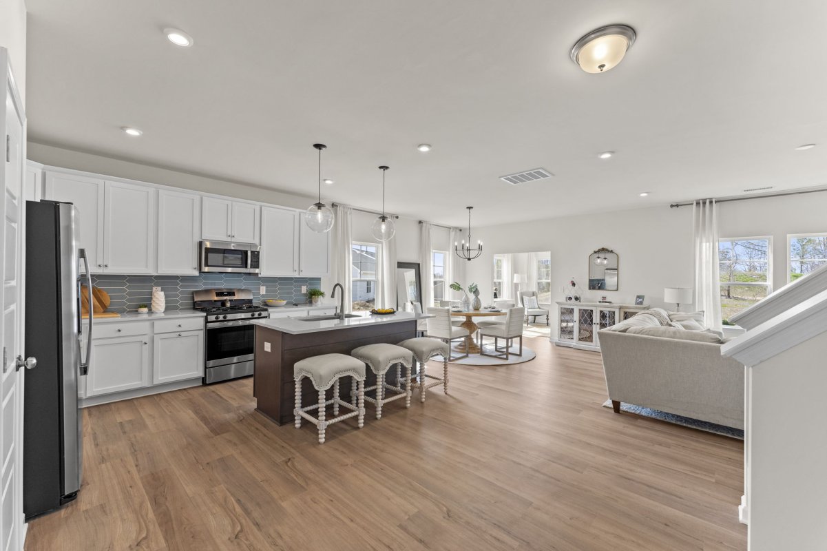 Open-concept kitchen and dining room in the Qualla Trace community by HHHunt Homes, featuring white cabinetry, stainless steel appliances, a large island with seating, and modern lighting.