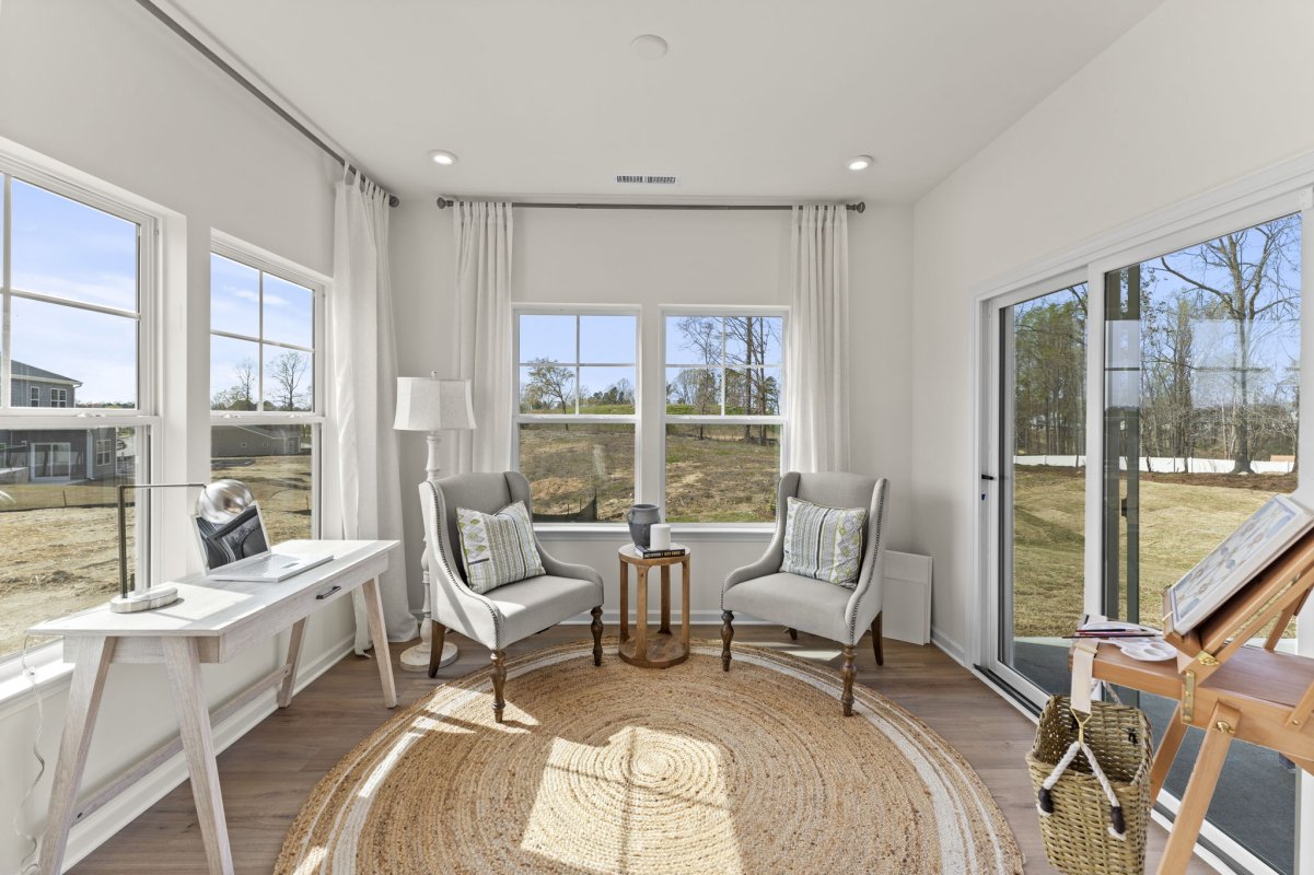 Flex room in the Curie floor plan by HHHunt Homes at Qualla Trace, featuring large windows, neutral tones, accent chairs, a small writing desk, and a cozy round jute rug with natural light for work or relaxation.