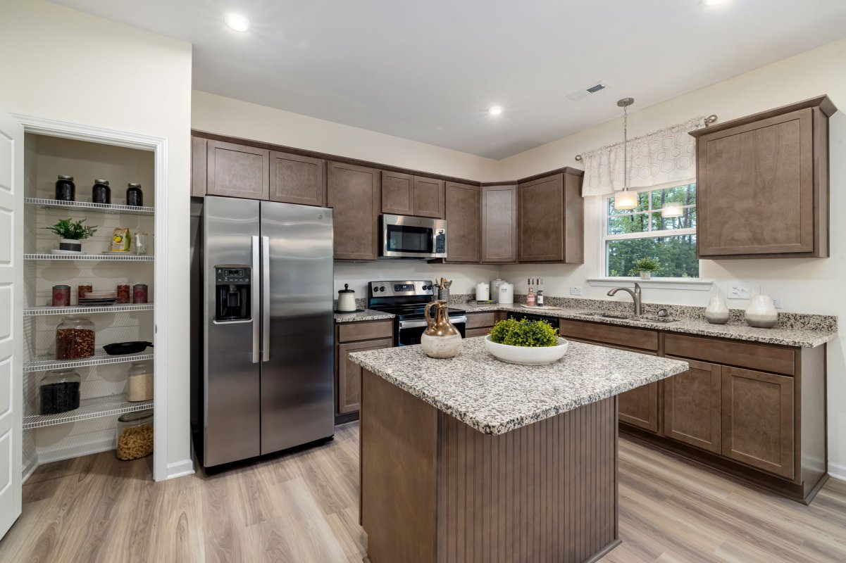 Kitchen in the Edison floor plan by HHHunt Homes at Qualla Trace, featuring wood cabinetry, granite countertops, stainless steel appliances, pantry, and center island with decorative accents.