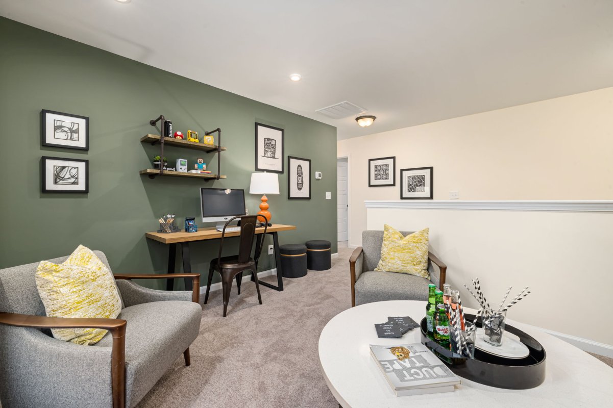 Loft space in the Edison floor plan at Qualla Trace by HHHunt Homes, featuring a desk with computer, cozy lounge seating, decorative shelving, and green accent wall.