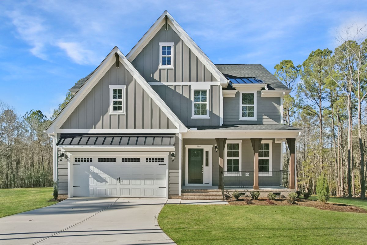 Front exterior of the Franklin floor plan, Farmhouse A elevation, by HHHunt Homes at Tyson's Trail Estates, featuring board and batten siding, black metal roof accents, a two-car garage, and a covered front porch with wood columns.