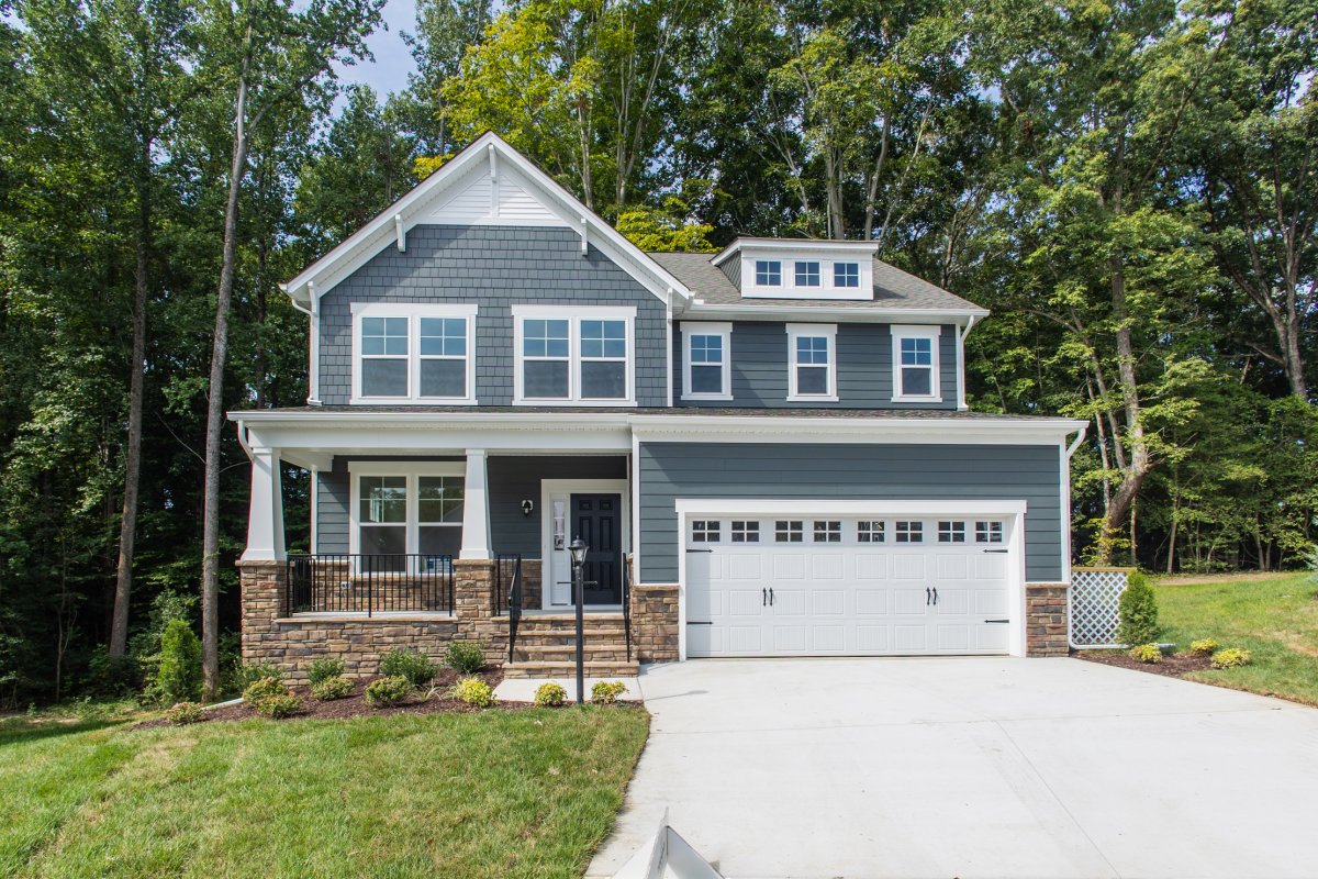 Front exterior view of the Chatham floor plan (Bungalow C elevation) at Tyson's Trail Estates by HHHunt Homes, featuring blue siding with white trim, a covered front porch, and two-car garage surrounded by mature trees.
