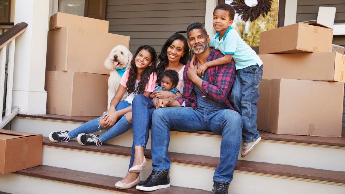 A family of five and their dog sitting on the front porch of their new home, surrounded by moving boxes.