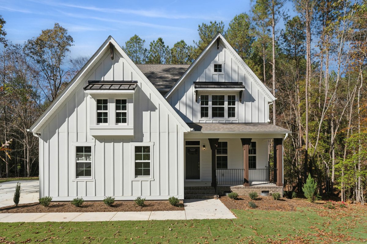 Exterior view of the Chatham Farmhouse A floor plan with sideload garage at Tyson’s Trail Estates by HHHunt Homes, featuring board and batten siding, a covered front porch, and wooded backdrop.