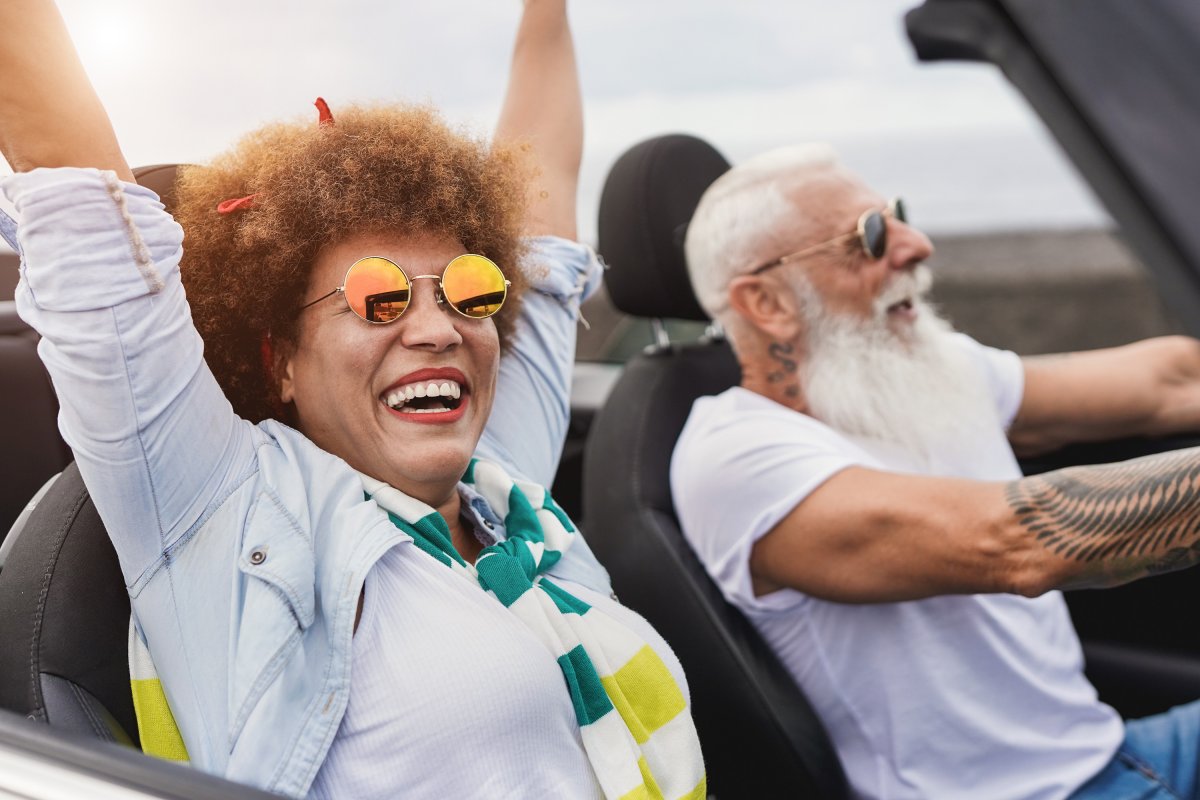A closeup of an older couple smiling while riding down the road in a convertible.