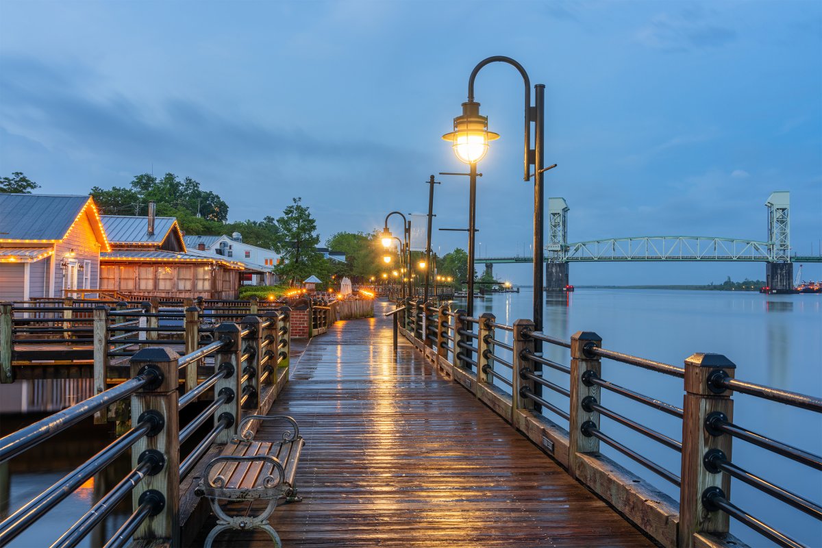 View down a pier at dusk in Wilmington, NC, with a bridge visible in the background.