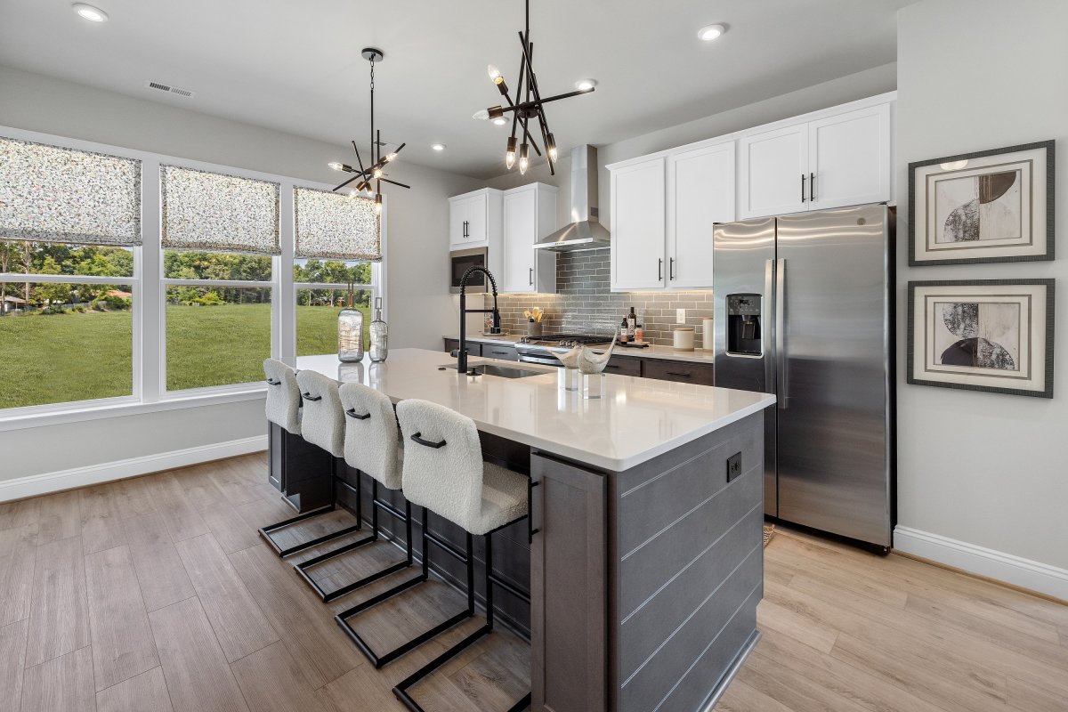 Modern kitchen in the Drake floor plan at The Aire At Westchester by HHHunt Homes, featuring a large island with quartz countertops, sleek black fixtures, two contemporary pendant lights, stainless steel appliances, white and gray cabinetry, and wide-plan