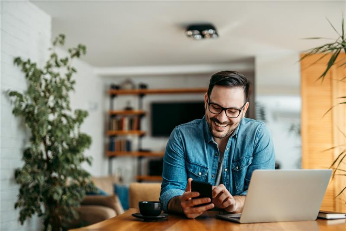 Smiling man sitting at a table with his laptop and phone