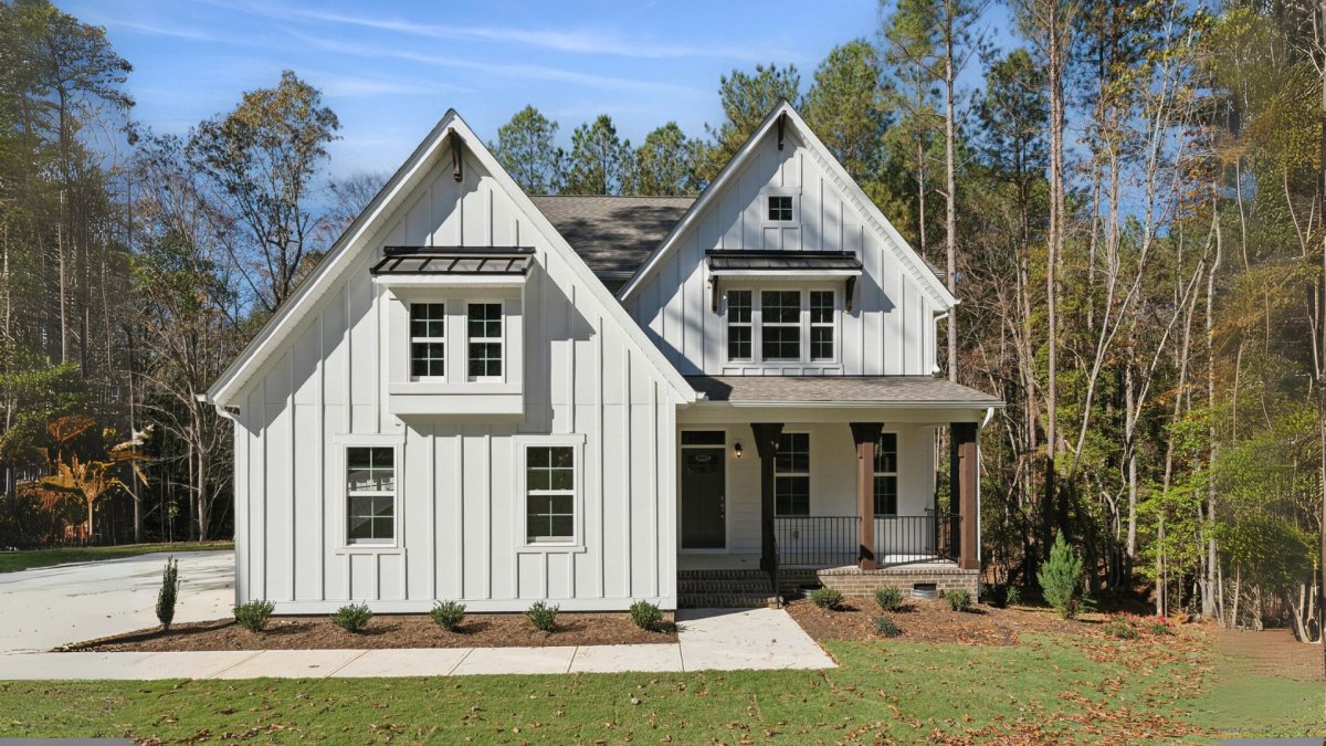 Exterior view of the Chatham Farmhouse elevation at Bethesda Forest by HHHunt Homes, featuring board and batten siding, gabled rooflines with metal accent roofs, a covered front porch with wood columns, and a landscaped front yard.