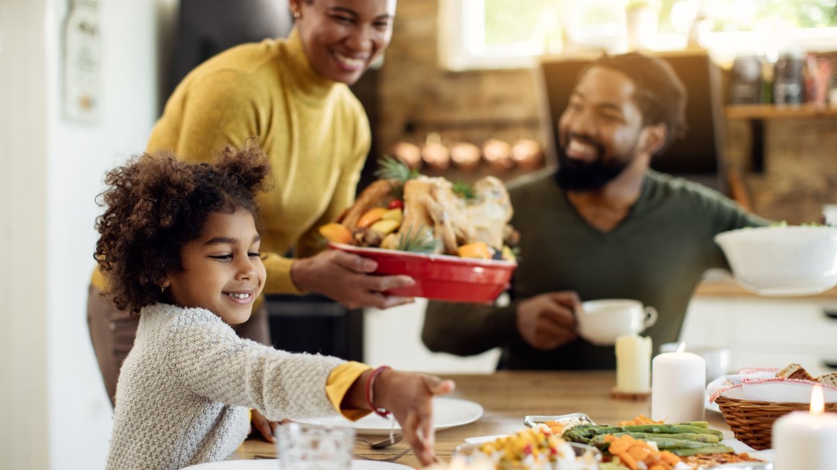A family of three having dinner in their home. Mom brings the main dish to the table