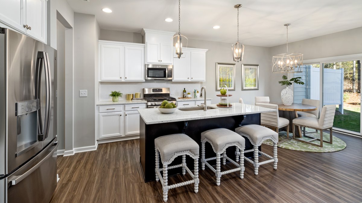Kitchen in a Mount Hermon townhome by HHHunt Homes featuring white cabinetry, stainless steel appliances, a large center island with quartz countertop and decorative stools, pendant lighting, and an adjoining dining area with sliding glass doors to the ba