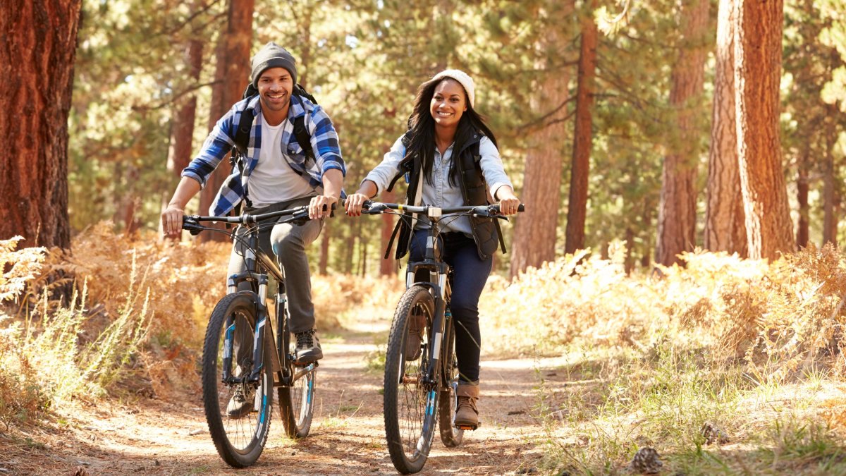 A couple smiling while mountain biking side by side on a trail through the woods
