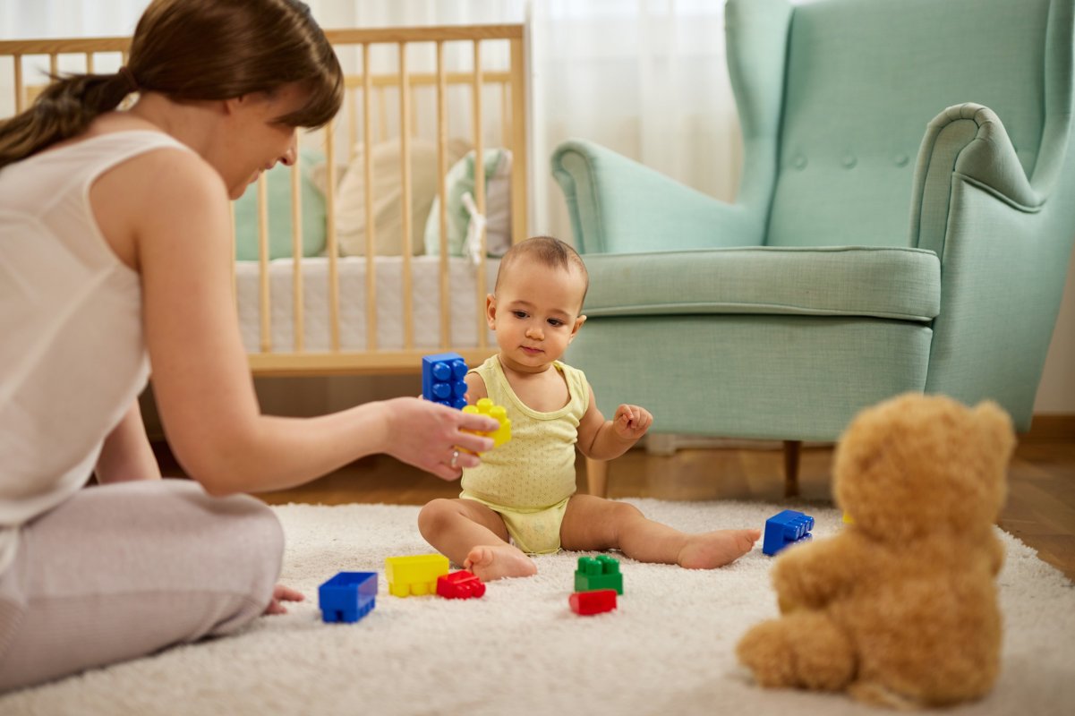 A mom sits on the floor with her baby while they play with legos