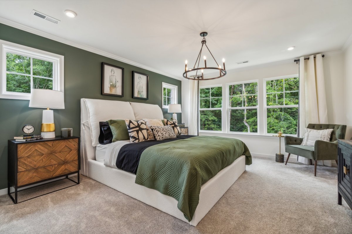 Primary bedroom in a Granite Ridge townhome by HHHunt Homes with upholstered bed, green accent wall, and chandelier.