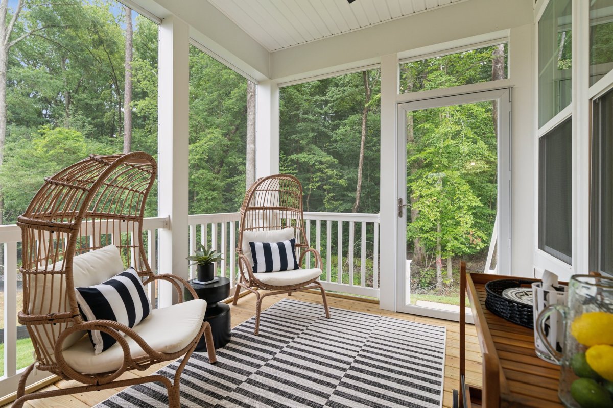 Screen porch in a Granite Ridge townhome by HHHunt Homes with wicker chairs, striped rug, and wooded views.