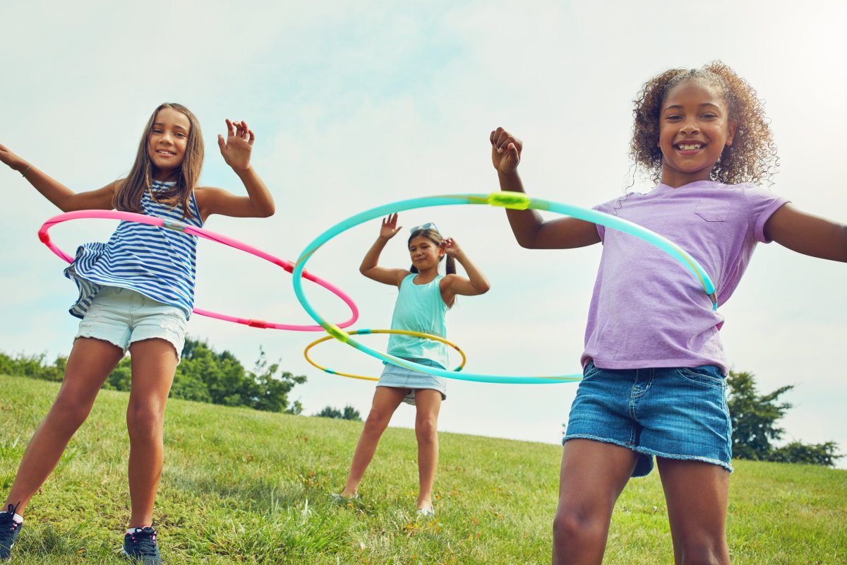 Three young girls hula hooping together in a large grassy field