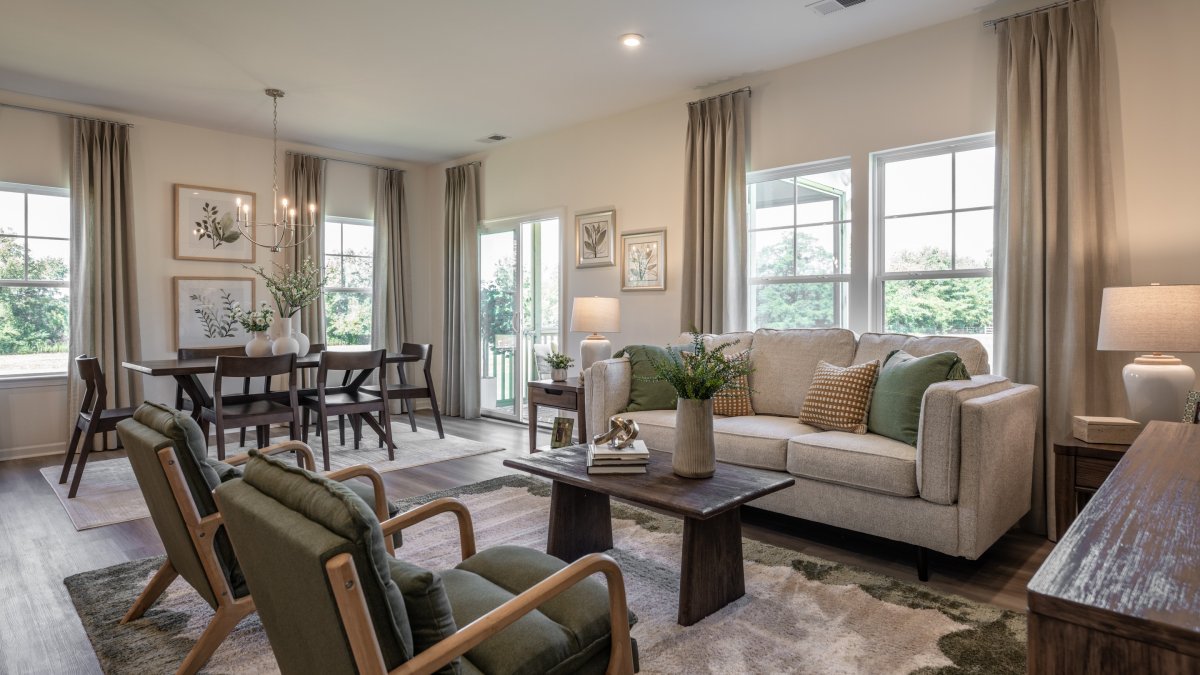 Family room in the Maxwell floor plan by HHHunt Homes at Oak Meadow, showcasing a beige interior with a sofa, rectangular wood coffee table, and modern chairs..