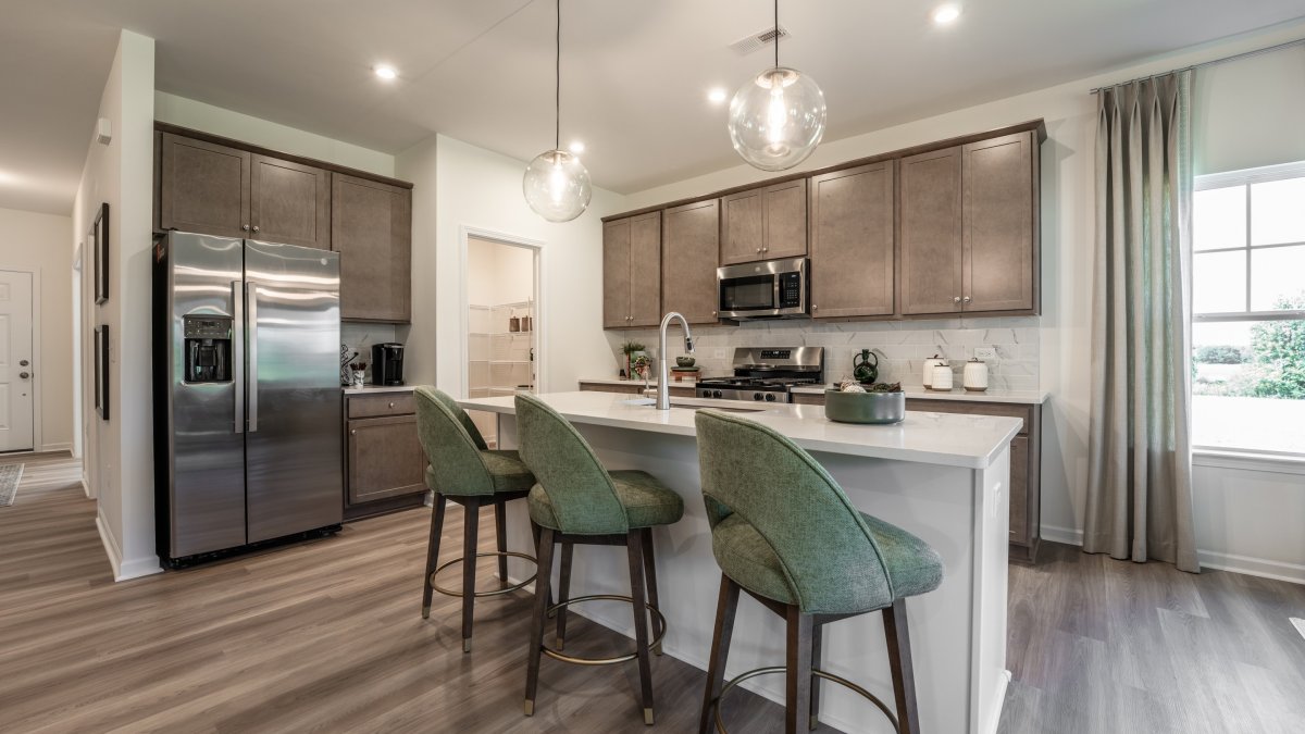 Open-concept kitchen area in the Maxwell floor plan by HHHunt Homes at Oak Meadow, with a central island featuring a sink and bar seating, ample natural light, and modern stainless steel appliances.
