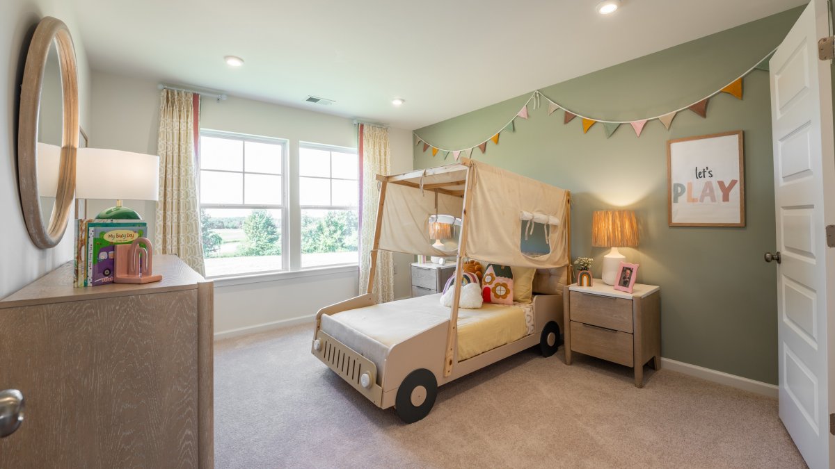 Children’s bedroom in the Maxwell floor plan by HHHunt Homes at Oak Meadow, featuring a car-frame bed with colorful bedding and play-themed decor, and a large window with natural light.