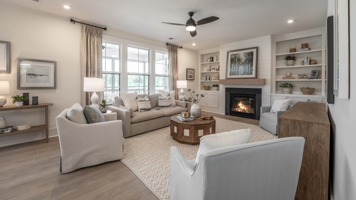 Open-concept living room in an HHHunt Home at Tyson's Trail Estates, featuring warm wood floors, neutral furniture with colorful accents, and natural light from large windows. Enjoy cozy evenings by the fireplace.Open-concept living room in an HHHunt Home