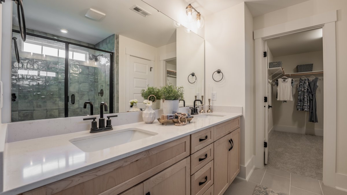 Primary bathroom in the Chatham floor plan at Tyson’s Trail Estates by HHHunt Homes, featuring a walk-in shower with textured wall tiles and a bench. Double vanity with light wood cabinetry, quartz countertops, and modern black fixtures.