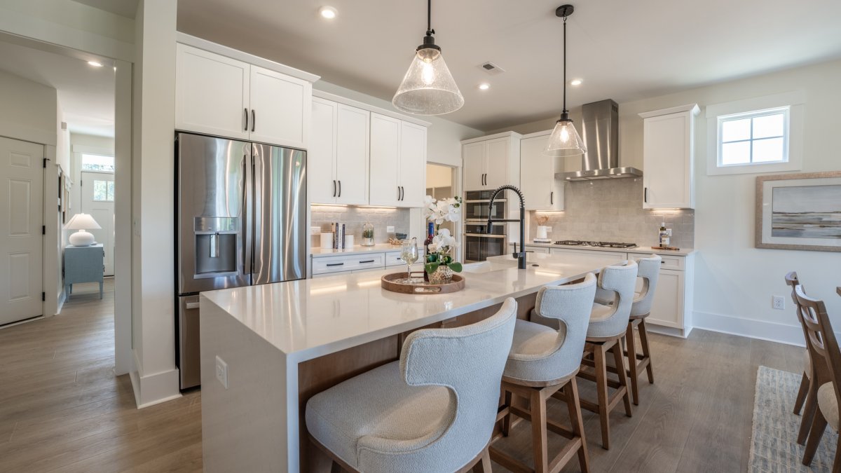 Kitchen in the Chatham floor plan at Tyson’s Trail Estates by HHHunt Homes, featuring a large waterfall island with bar seating, pendant lighting, white cabinetry, and stainless steel appliances.