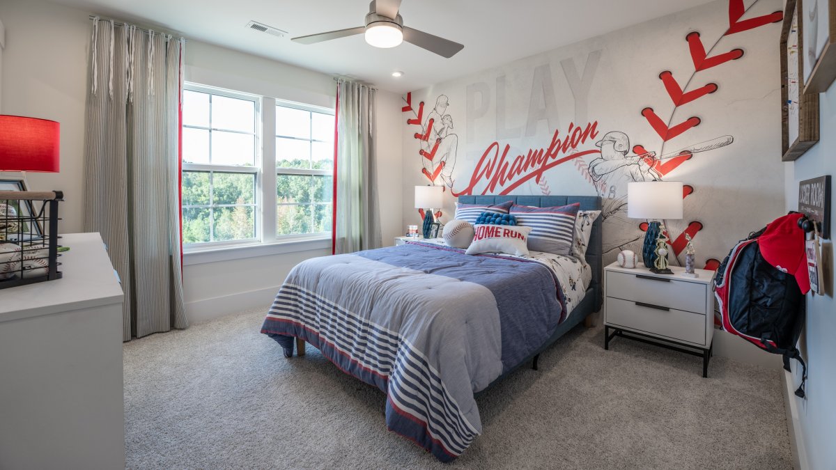 Bedroom in the Chatham floor plan at Tyson's Trail Estates by HHHunt Homes, featuring a baseball themed room with a full bed with room for a nightstand. Enjoy tons of natural light from the double windows and a breeze from the ceiling fan.
