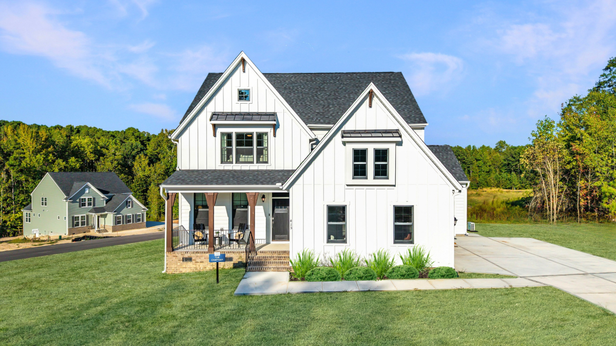 xterior view of the Chatham Farmhouse A floor plan with sideload garage at Tyson’s Trail Estates by HHHunt Homes, featuring board and batten siding, a covered front porch, and large lot with a backdrop.