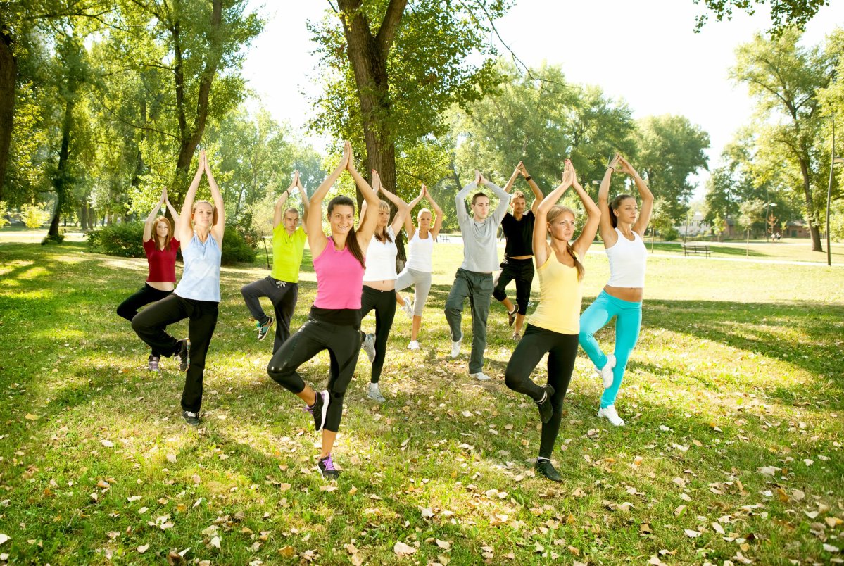 A group of ten young adults doing yoga in a grassy field