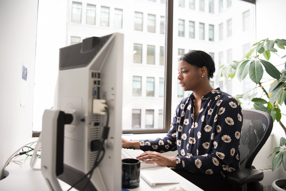 Woman working at a desktop computer in a modern office with large windows and natural light.