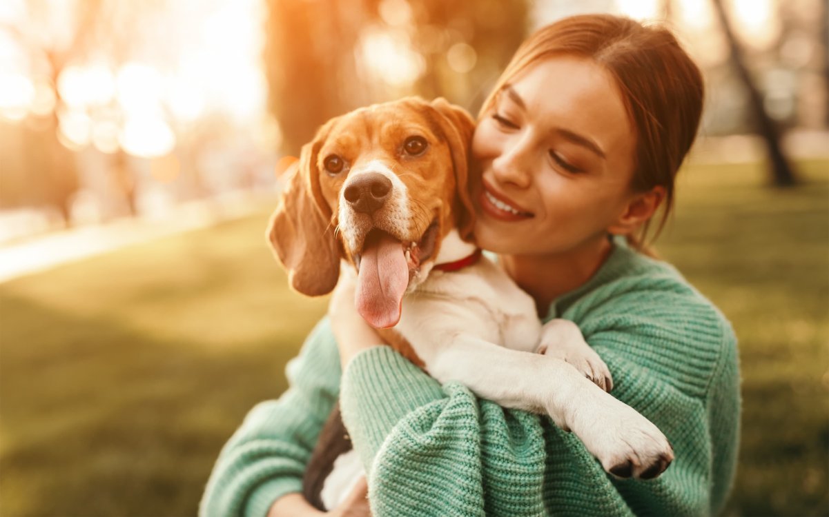A young woman holds her dog while sitting in a grassy field