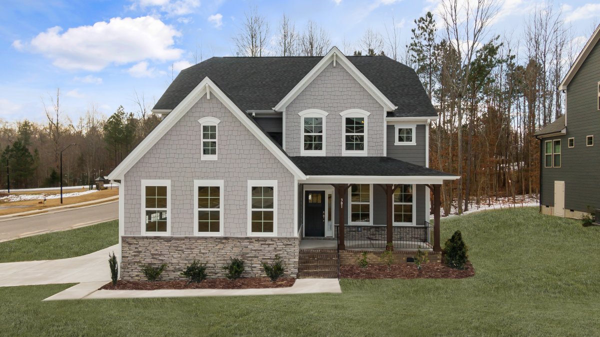 Two-story European-style home with side-entry garage in Oak Meadow by HHHunt Homes, featuring gray siding, stone accents, and a covered front porch.